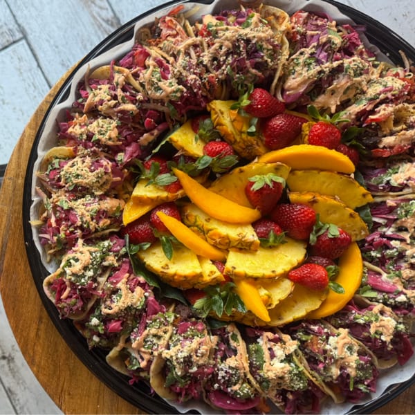 A platter of Strive Foods tacos with red cabbage, sauce, and a center of pineapple, mango, and strawberries.