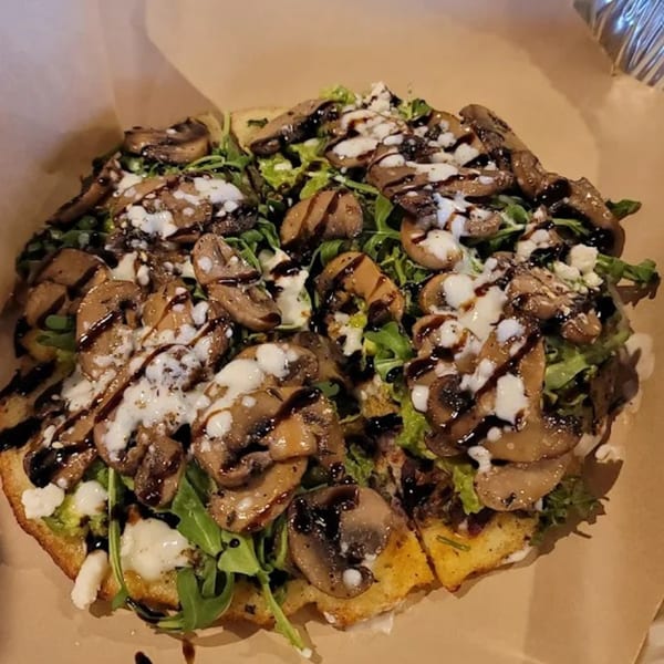 A healthy flatbread pizza topped with mushrooms, arugula, cheese, and balsamic glaze.