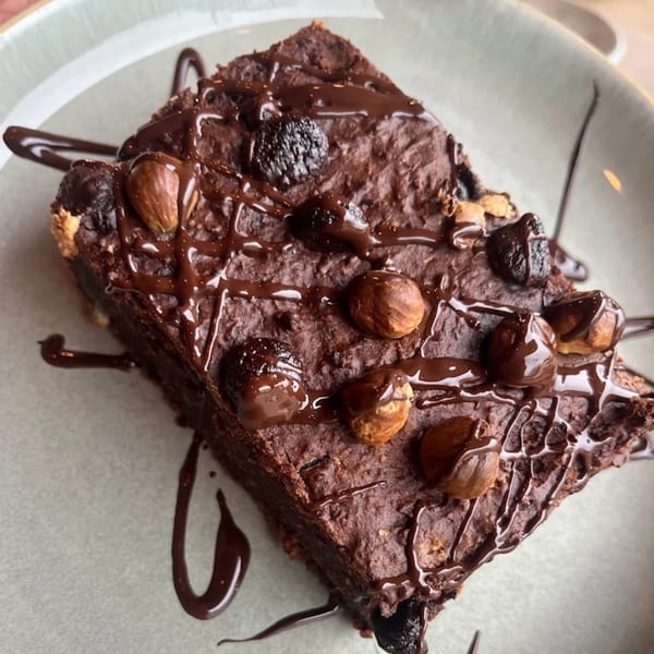 A healthy chocolate brownie from Strive Foods, drizzled with chocolate sauce and topped with nuts and berries.