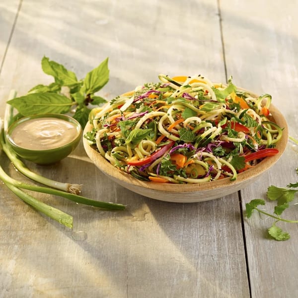 A vibrant Strive Foods healthy noodle salad with dressing, basil, and green onions on a wooden table.
