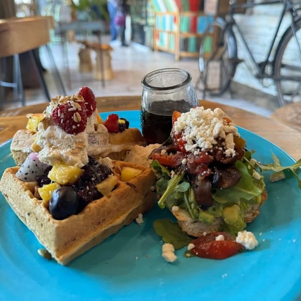 Sweet fruit waffles with whipped cream and savory avocado toast with feta on a blue plate.